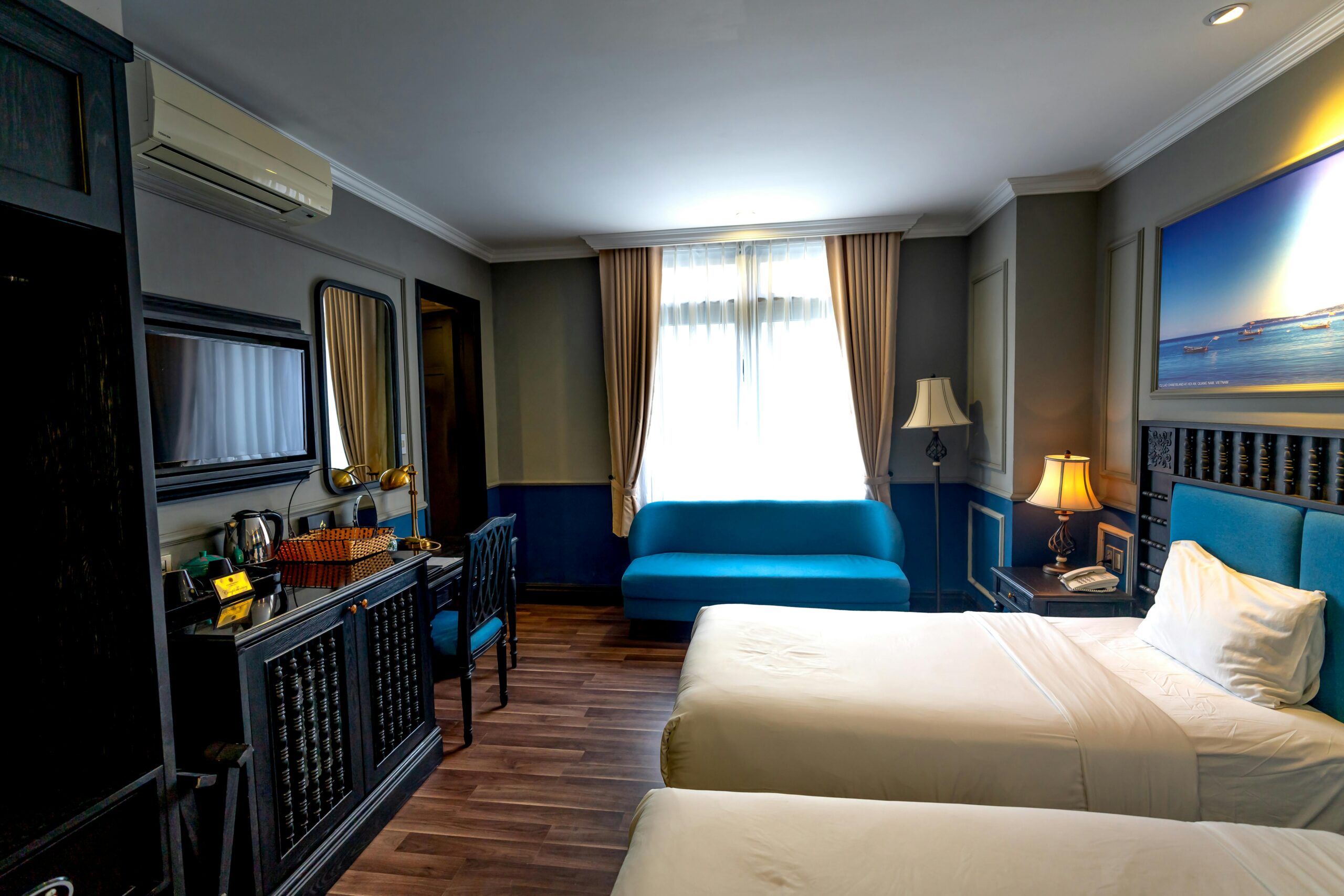 Luxurious hotel room featuring two beds, a blue sofa, artwork, and contemporary furniture.